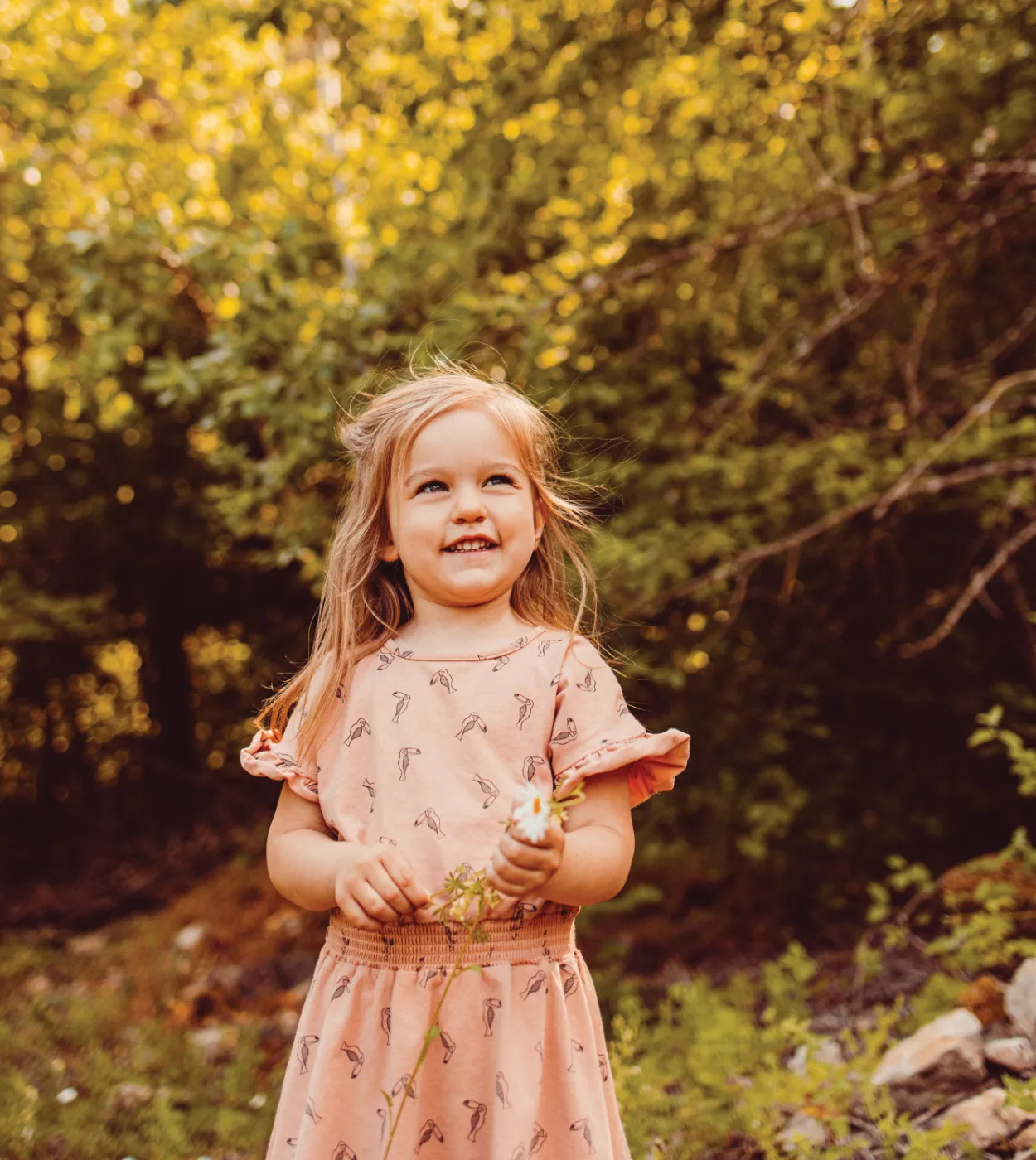 Kleines blondes Mädchen in rosa Kleid mit einer Gänseblume