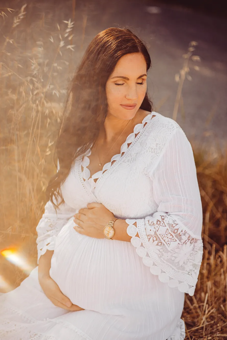 Schwangere Frau in weißen Kleid hält Ihre Hände auf ihren Babybauch responsive.
