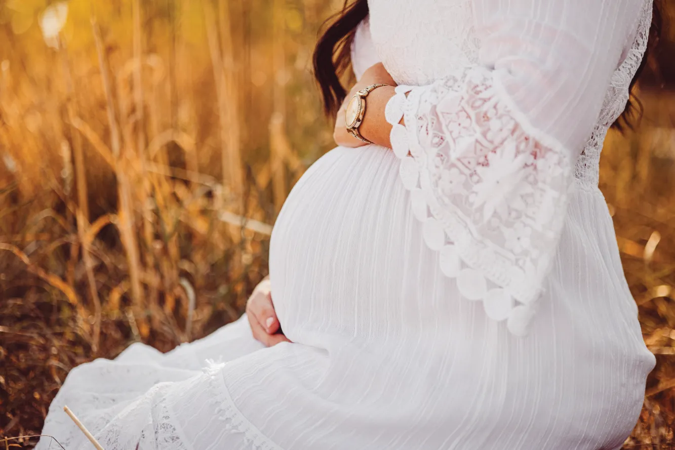 Schwangere Frau in weißen Kleid hält Ihre Hände auf ihren Babybauch, Ausschnitt